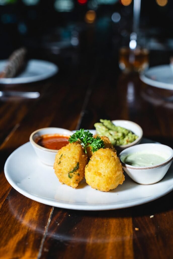 "Marranitas caleñas gourmet rellenas de chicharrón y coronadas con guacamole fresco, presentadas en un bowl de vidrio sobre mesa oscura con fondo de bar o restaurante."
