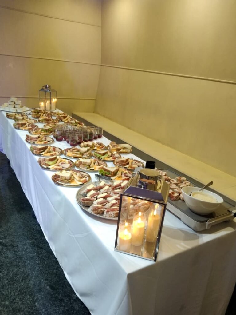 Mesa de banquete empresarial en Bogotá con tabla de quesos gourmet, candelabros de lujo y mantelería blanca, servida por Rocha's Catering con logística de alta gama.